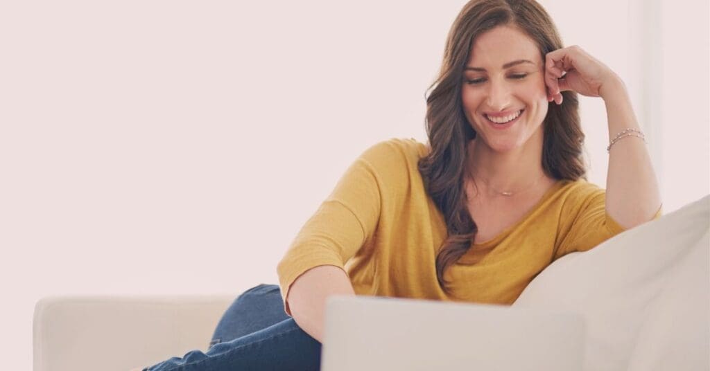 Female entrepreneur smiling while working on laptop, learning how to think like a CEO as an entrepreneur.