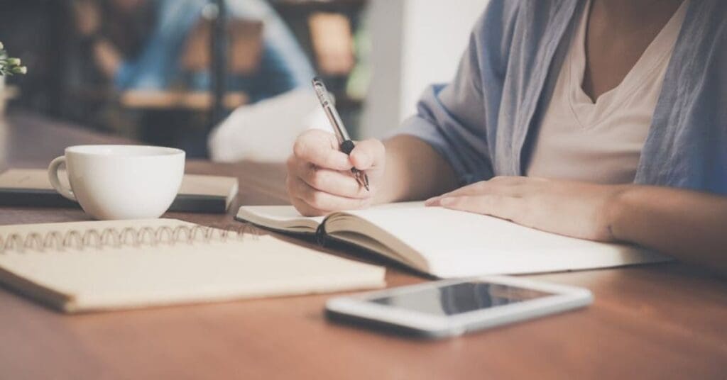 Entrepreneur journaling business goals and CEO vision with coffee at a cozy workspace.