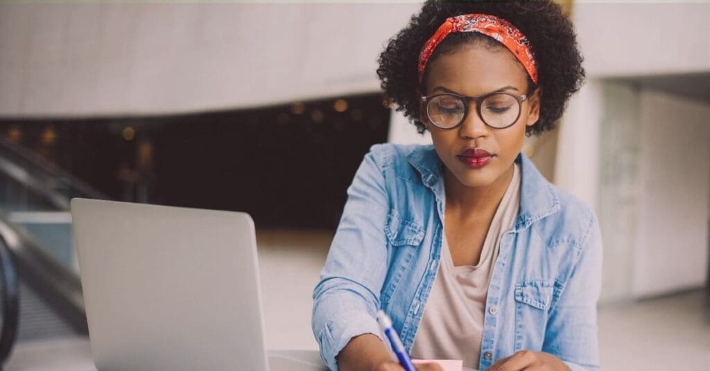 Focused entrepreneur planning business strategy on laptop and taking notes.